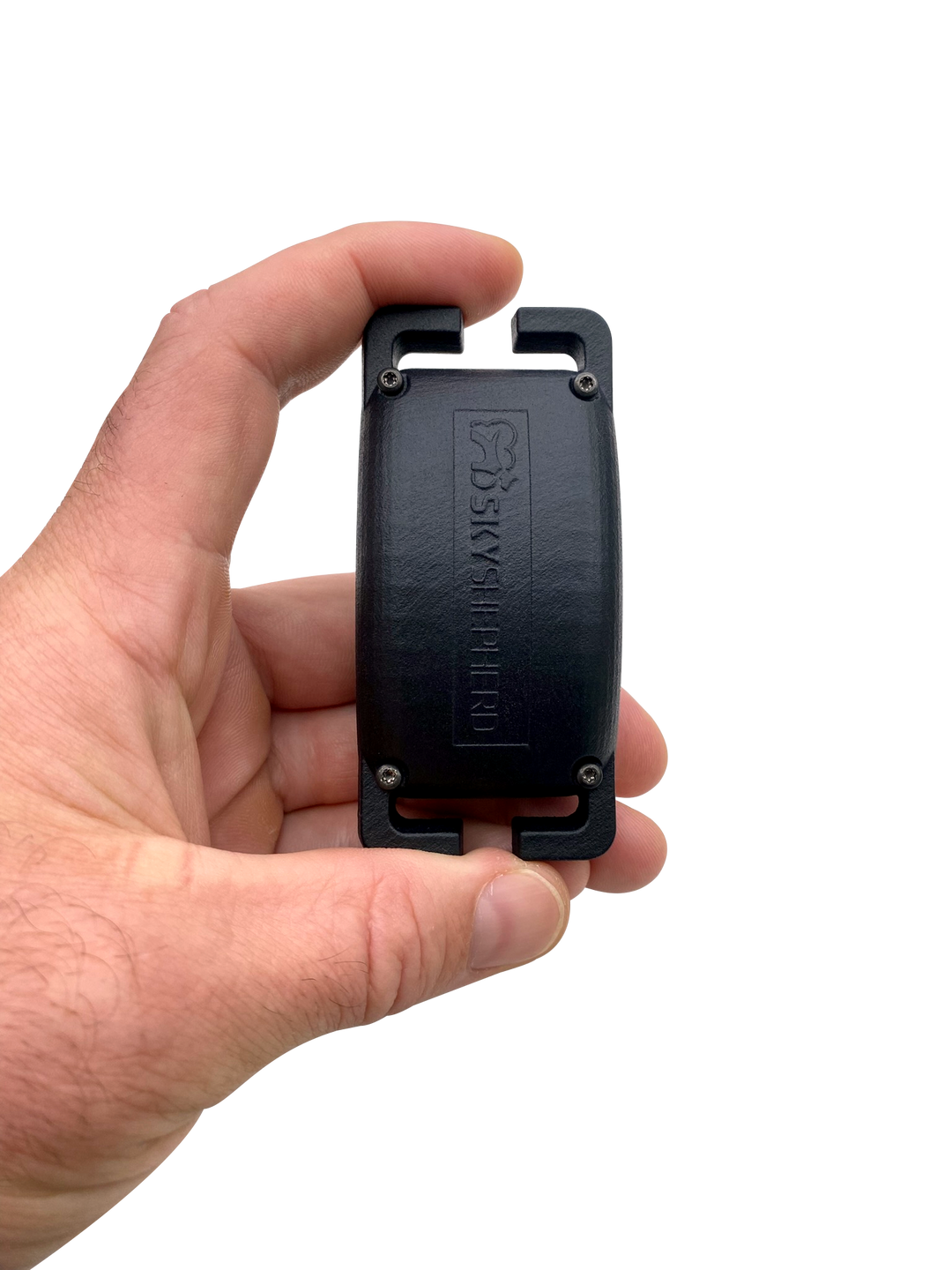 A hand holds the SkyShepherd collar between thumb and index finger. The collar is being held lengthwise, from bracket to bracket, end to end. The SkyShepherd logo appears engraved on the convex surface of the collar unit. 