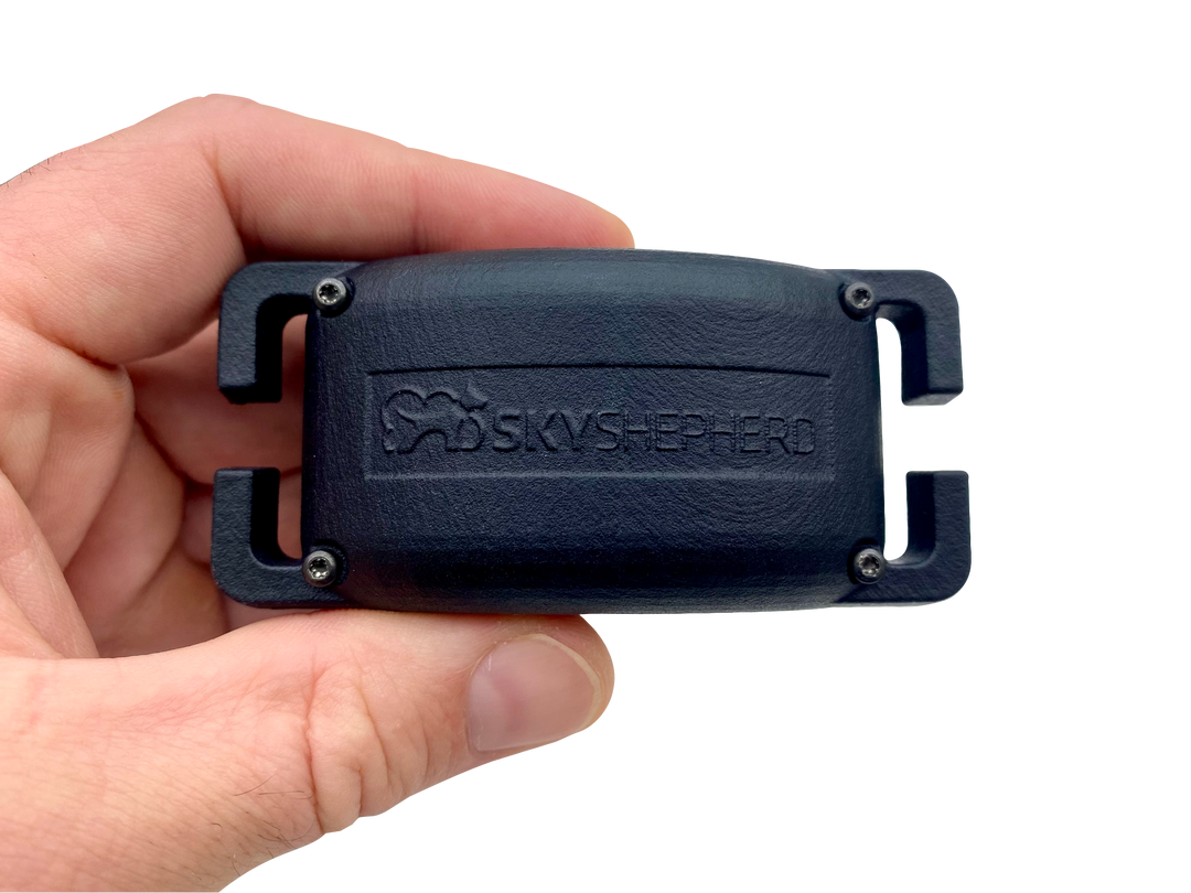 SkyShepherd GPS collar unit is held horizontally between thumb and index finger. The SkyShepherd Logo can be seen embossed on the surface of the collar unit. 