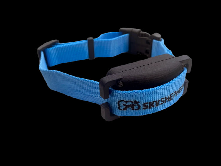 The black plastic SkyShepherd GPS collar unit is shown from a three-quarters oblique angle from the right front. The branded SkyShepherd light blue collar strap is attached to the collar unit through the integrated brackets on either end of the collar unit. The black SkyShepherd logo, including the dog-in-cloud portion, is visible to the viewer, embroidered in the SkyShepherd blue nylon collar strap.